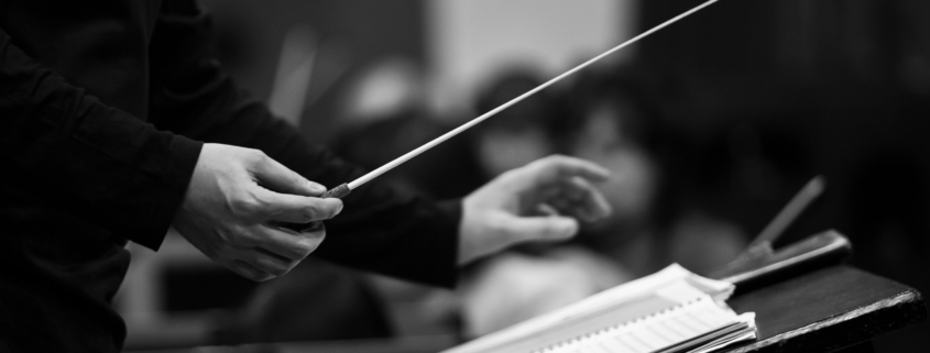 An orchestral conductor holds a baton above some sheet music