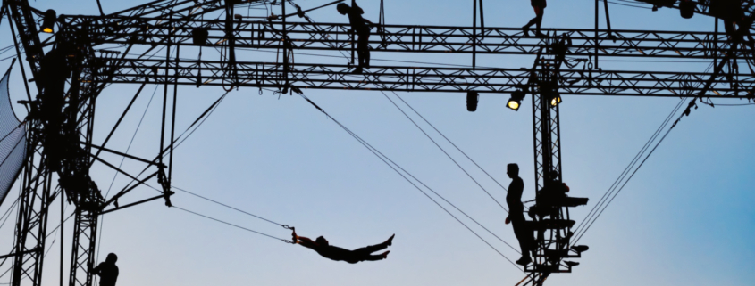 A silhouette of flying trapeze artists and a framework construction